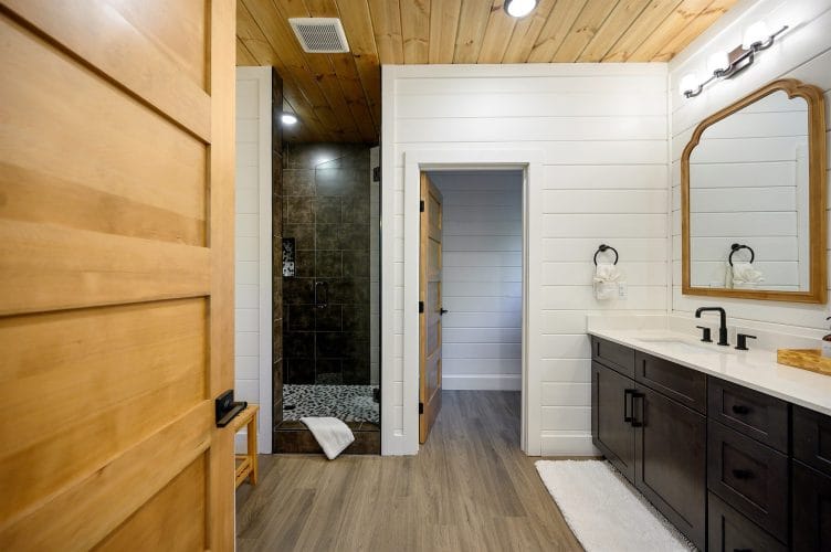 Bathroom with a dark double vanity and a tiled walk-in shower beyond