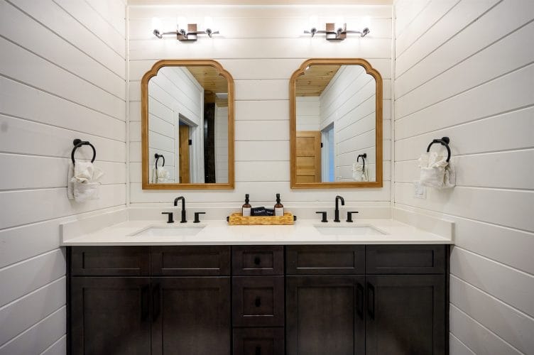 Double vanity with two wood-framed mirrors and black faucets