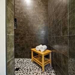 Tiled walk-in shower with a wooden stool and rolled towels