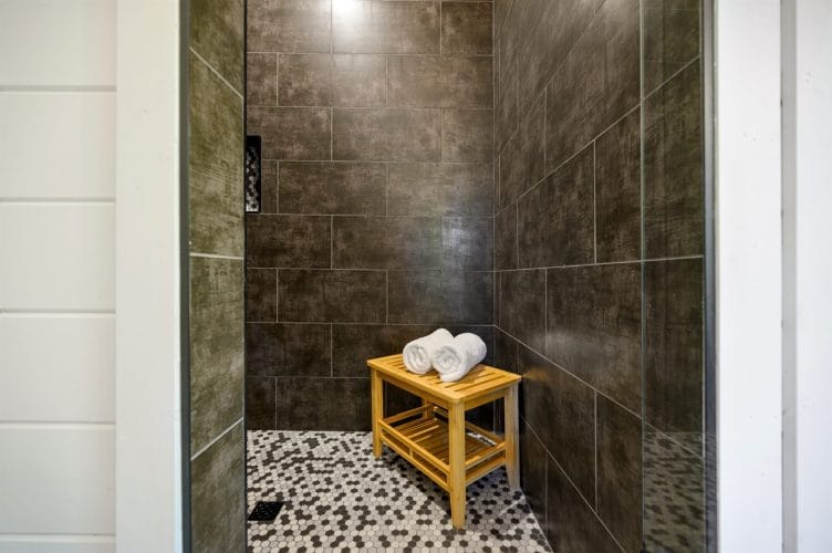 Tiled walk-in shower with a wooden stool and rolled towels
