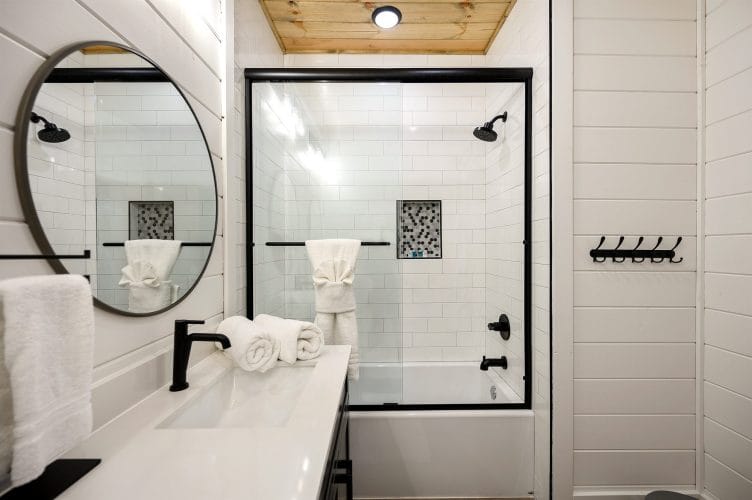 Bathroom with a tub-and-shower, a round mirror and black fixtures
