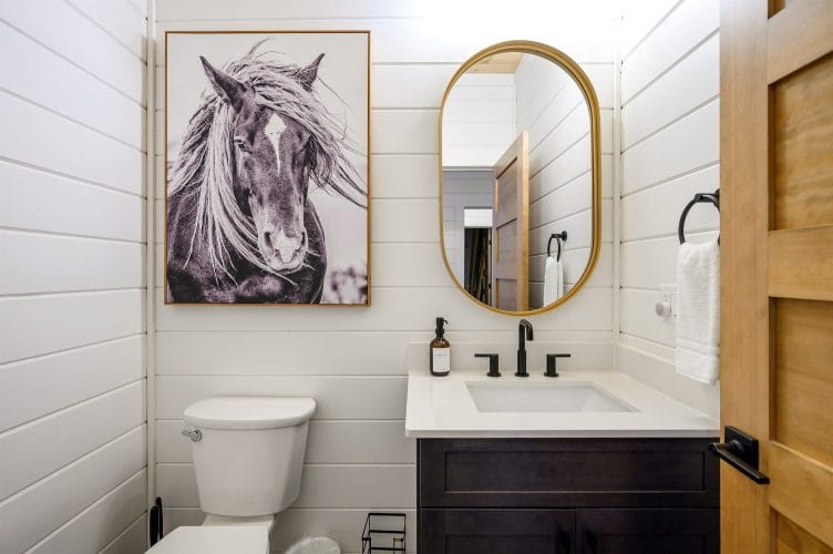 Half bath with a framed horse print, a dark vanity and an oval gold mirror