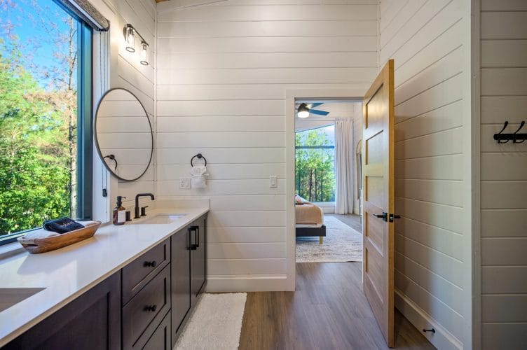 Bathroom with a long dark vanity, a round mirror and a window