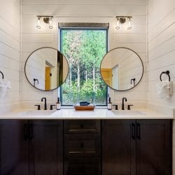 Double vanity with two round black-framed mirrors and a window between them