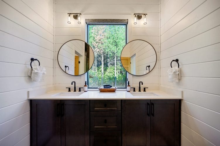 Double vanity with two round black-framed mirrors and a window between them