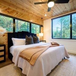 King bed with a black upholstered headboard under a pine plank ceiling, windows along the wall