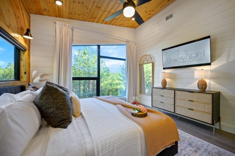 King bed with a TV on the wall, a dresser and a ceiling fan
