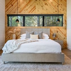 Bed against a herringbone pine accent wall with pendant lights and a long window