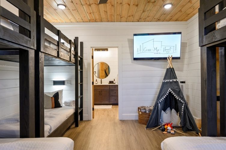 Bunk room with black wood bunks, a wall TV and a gray canvas teepee