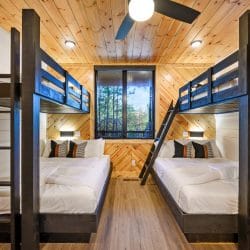 Two stacks of black wood bunks under a pine ceiling, with a window between them