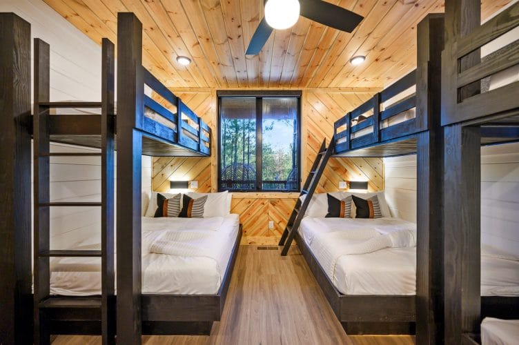 Two stacks of black wood bunks under a pine ceiling, with a window between them