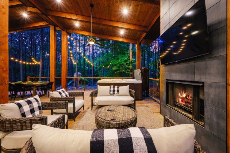 Covered patio with a tile fireplace burning, a big TV and wicker lounge seating
