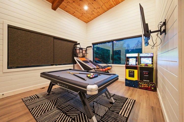 Game room with a pool table, arcade cabinets and a basketball game under a plank ceiling