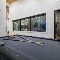 Pool table with cue sticks and a glass door to the deck