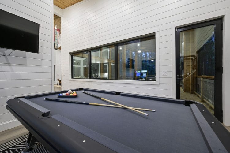 Pool table with cue sticks and a glass door to the deck