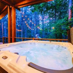 Hot tub on a covered deck among tall pines, with string lights beyond the rail