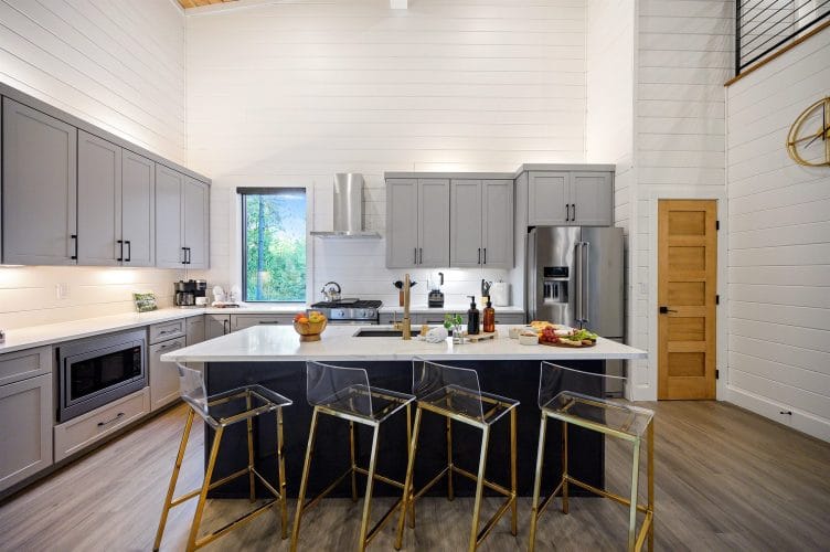 Kitchen with gray cabinets and a white island with four clear stools