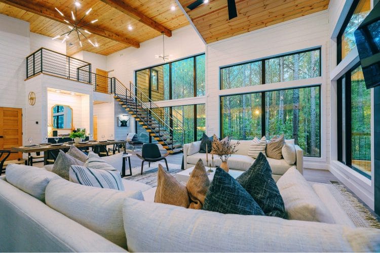Great room with a two-story ceiling, an open staircase, a wall of windows and a long white sofa