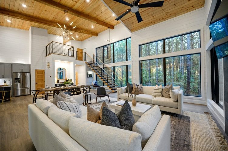 Great room with sofas, a TV and the stair railing under a tall plank ceiling