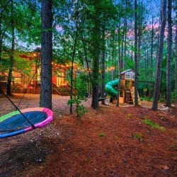 Nest swing and the playset in the pines, with the cabin lit up behind