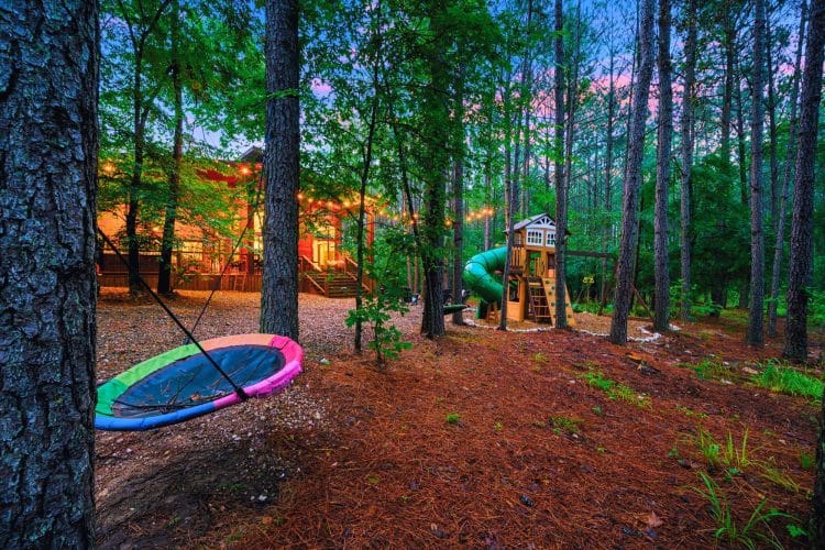 Nest swing and the playset in the pines, with the cabin lit up behind