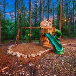 Playset with a green slide and a wooden tower, ringed with rocks