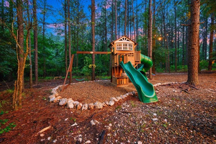 Playset with a green slide and a wooden tower, ringed with rocks