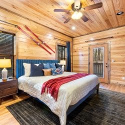 King bed with a blue headboard and a red throw, skis on the wall