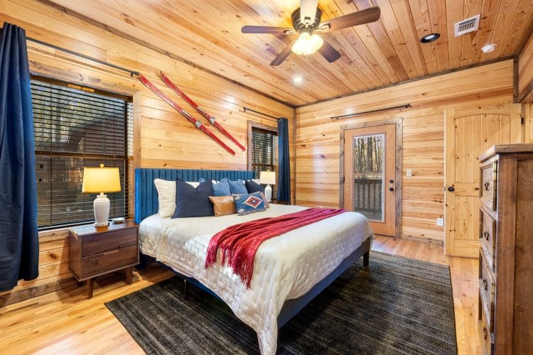 King bed with a blue headboard and a red throw, skis on the wall