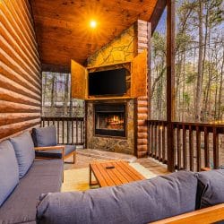 Covered porch with a stone fireplace, a TV and a gray sectional