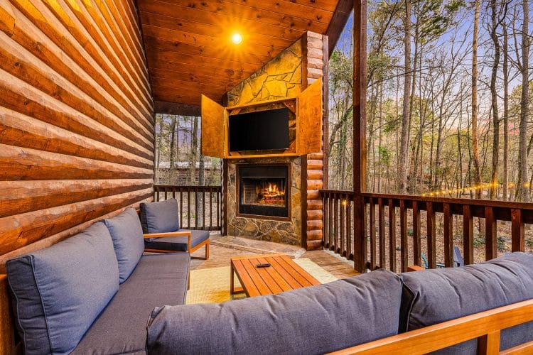 Covered porch with a stone fireplace, a TV and a gray sectional