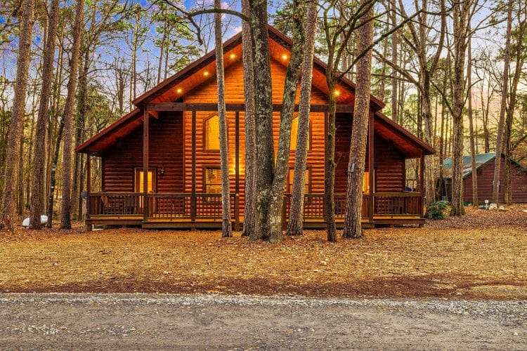 Log cabin with a covered porch among tall pines in the evening