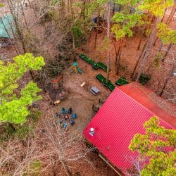 Aerial view of the red metal roof, mini golf course and fire pit in the woods