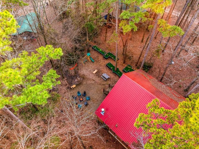 Aerial view of the red metal roof, mini golf course and fire pit in the woods