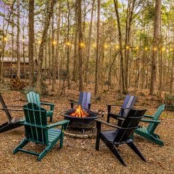 Fire pit with green and black Adirondack chairs under string lights