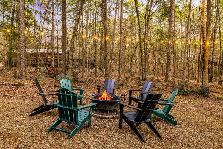 Fire pit with green and black Adirondack chairs under string lights