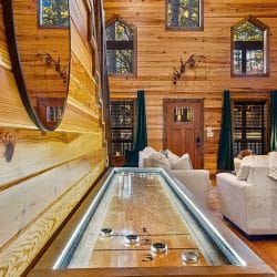 Lit shuffleboard table in the living room with the stone fireplace beyond