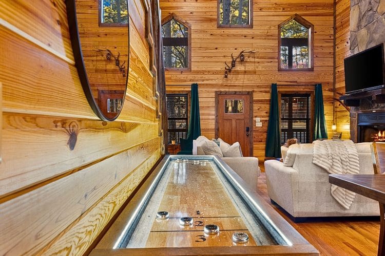 Lit shuffleboard table in the living room with the stone fireplace beyond