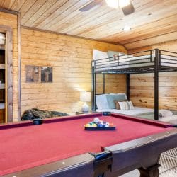 Pool table with red felt in front of the bunk beds and a shelf of games