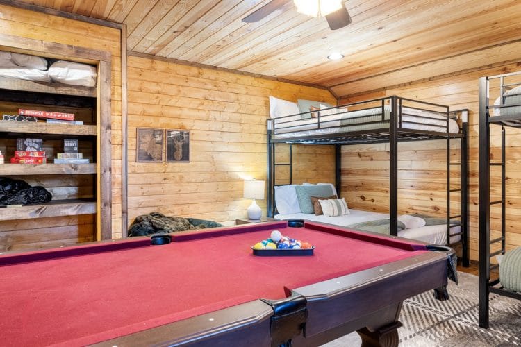 Pool table with red felt in front of the bunk beds and a shelf of games