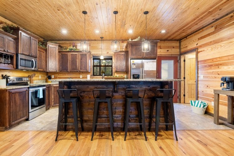 Kitchen with an island bar, four black stools and wood cabinets