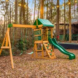 Wooden playset with a green slide in the woods