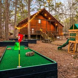 Mini golf hole with a red flag, the playset and the cabin behind