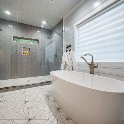 Freestanding soaking tub beside a glass walk-in shower with herringbone tile