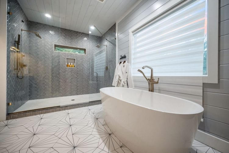 Freestanding soaking tub beside a glass walk-in shower with herringbone tile