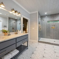 Double vanity with gold faucets and a large herringbone-tile walk-in shower