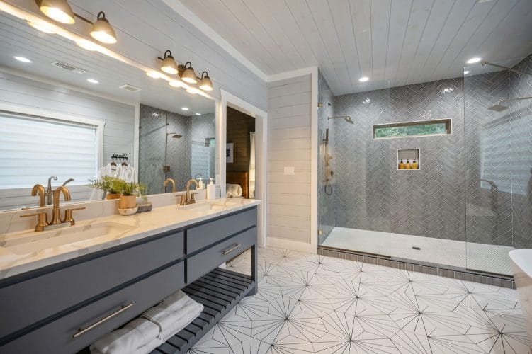Double vanity with gold faucets and a large herringbone-tile walk-in shower