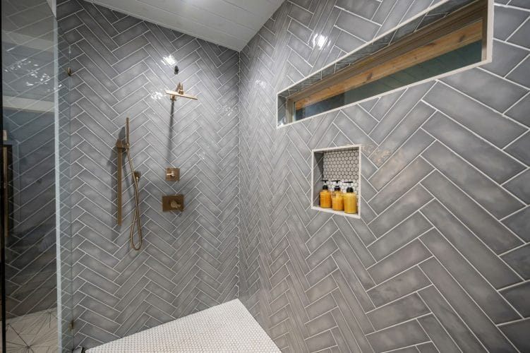 Walk-in shower with gray herringbone tile and a long window niche