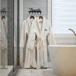 White bathrobes hung beside the tub under a Towels sign