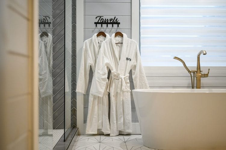 White bathrobes hung beside the tub under a Towels sign